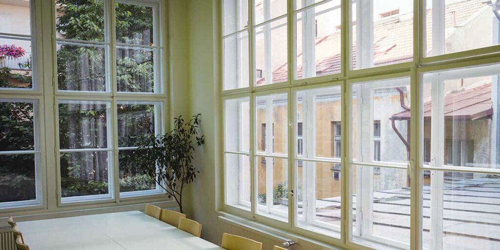 A bright room featuring large white-framed paneled windows, highlighting choices for pocket and full frame window replacement options.